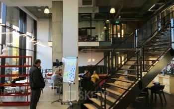 Modern office space rental at Arthur van Schendelstraat 650, Utrecht Central Station, featuring open workspaces, stairs, and people engaged in discussions.