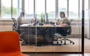 Modern office space rental at Leidseveer 2-10 in Utrecht Central Station with two people working at desks in a glass-walled room.