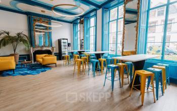 Stylish open floor plan office space rental at Kromme Nieuwegracht 3 in Utrecht Center, featuring blue and yellow decor, modern furnishings, and natural light from large windows.