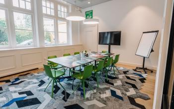Conference room at Kromme Nieuwegracht 3 in Utrecht Center with a table, green chairs, large windows, TV, and a flipchart.