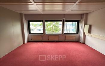 Interior view of an unfurnished office space available for rent at Bernadottelaan 13, Utrecht Kanaleneiland, featuring carpet flooring and large windows.