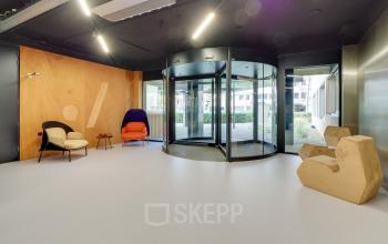 Spacious entrance area with modern revolving doors at Europalaan 400, Utrecht Kanaleneiland, ideal for office space rental. Minimalist chairs provide a welcoming touch to the sleek environment.