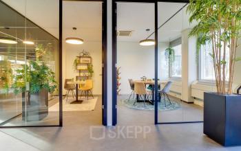 Bright and modern office space rental at Europalaan 400, Utrecht Kanaleneiland featuring glass-partitioned meeting rooms with plants and stylish furniture, ideal for collaborative work.