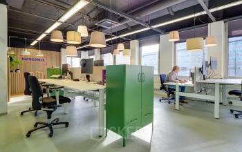 Modern workspace for office space rental at Europalaan 500, Utrecht Kanaleneiland. Features ample natural light, open plan desks, and vibrant decor with individuals working on computers and documents.