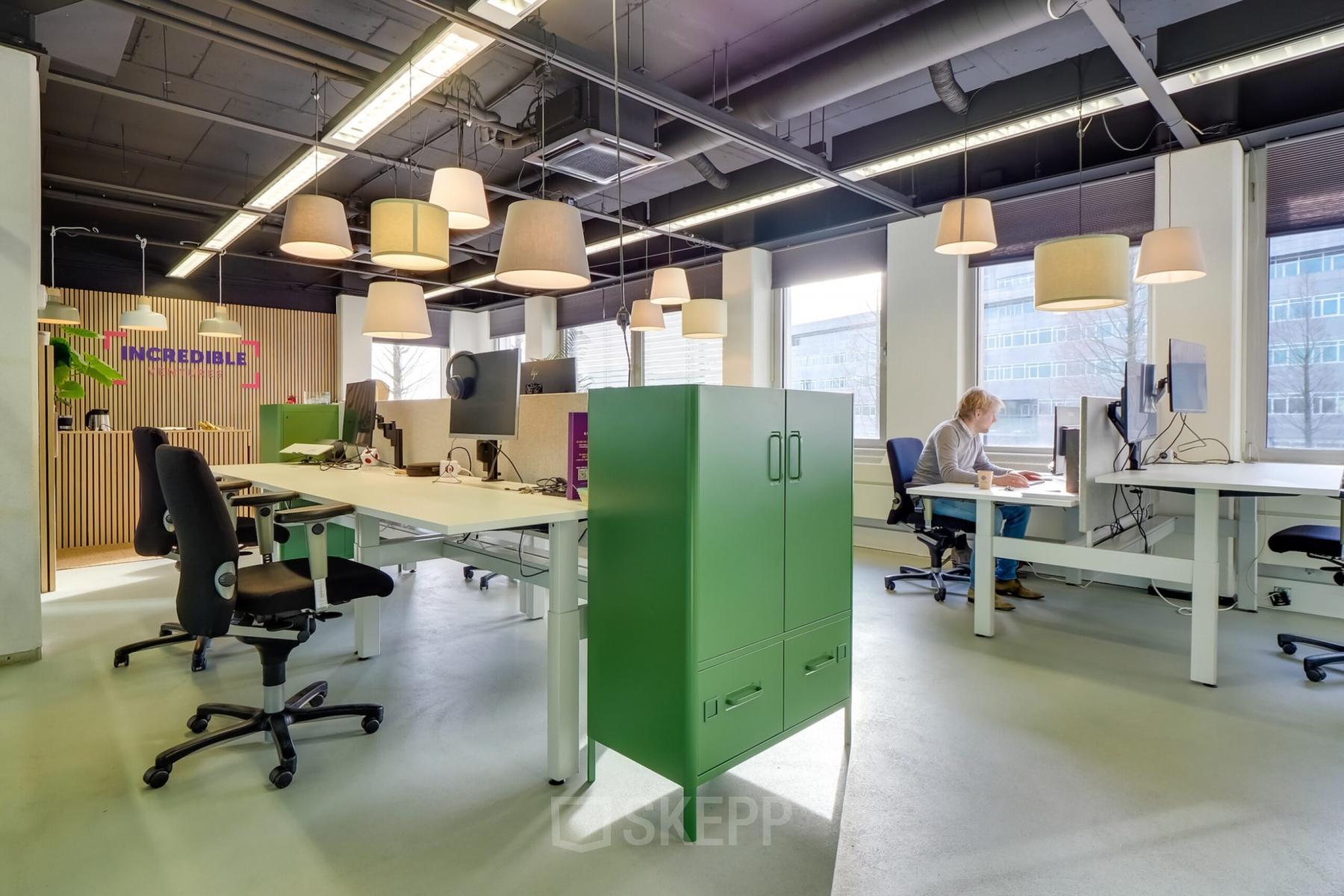 Modern workspace for office space rental at Europalaan 500, Utrecht Kanaleneiland. Features ample natural light, open plan desks, and vibrant decor with individuals working on computers and documents.