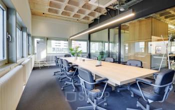 Modern conference room at Europalaan 101, Utrecht Kanaleneiland, featuring a long wooden table, office chairs, and glass partitions. Ideal for office space rental, this room offers a professional setting with ample natural light.