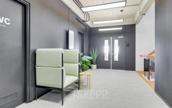 A modern corridor in an office building at Europalaan 101, Utrecht Kanaleneiland, featuring stylish seating and vibrant green plants, offering potential for office space rental.