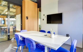Bright meeting room with blue chairs and a long white table, featuring a wall-mounted screen, located at Europalaan 101, perfect for office space rental in Utrecht Kanaleneiland.
