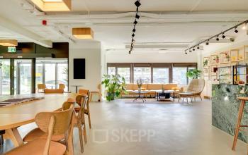 Bright and modern office space in Utrecht Kanaleneiland with stylish furniture, wooden tables, and large windows. Ideal for office space rental, this inviting workplace offers a relaxed ambiance and ample natural light.