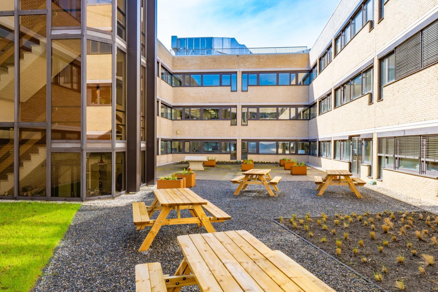 Courtyard view of the office building at Europalaan 93 in Utrecht Kanaleneiland, featuring outdoor seating and modern architecture, ideal for refreshing breaks. Perfect office space rental opportunity.