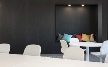 Modern office space in Europalaan 100, Utrecht Kanaleneiland, featuring sleek tables and colorful cushioned seating area. Ideal for office space rental.