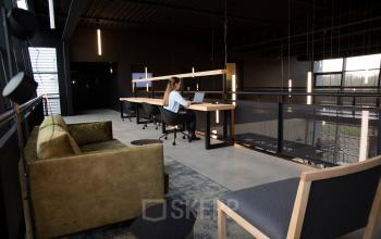 Modern office space rental at Atoomweg 63, Utrecht Lage Weide, featuring a stylish open floorplan with cozy seating and workstations where a person is working on a laptop.