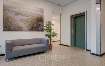Reception area at Zonnebaan 45 in Utrecht Lage Weide, featuring a comfortable sofa, nature artwork, and an elevator, ideal for office space rental.