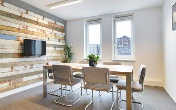 Office space for rent at Middenburcht 136, Utrecht Leidsche Rijn. A bright meeting room with a large wooden table, six chairs, wall-mounted TV, and a decorative wooden accent wall.