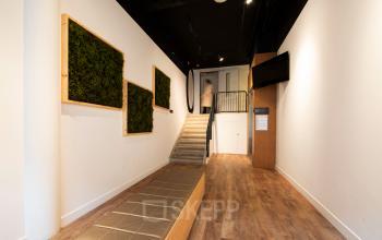 Modern office interior at Middenburcht 136 in Utrecht Leidsche Rijn, featuring wooden flooring, decorative wall art, and a staircase with a person ascending. Ideal for office space rental with easy access.