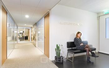 Hallway view of Middenburcht 136 office space in Utrecht Leidsche Rijn, featuring a woman seated on a bench beside potted plants.