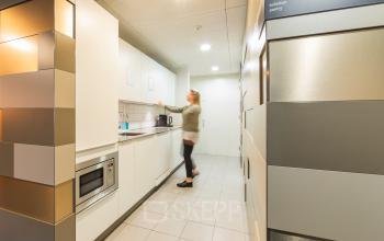 Person preparing a beverage in the pantry of an office located at Middenburcht 136, Utrecht Leidsche Rijn. Ideal for those seeking office space rental.