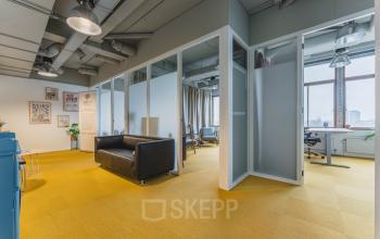 Spacious and bright workspace with modern decor, featuring yellow flooring, a black sofa, and large windows for natural light at Goeman Borgesiuslaan 77, ideal for office space rental in Utrecht North.