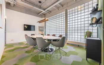 Modern conference room with stylish chairs and geometric carpet at office space rental on Goeman Borgesiuslaan 77, Utrecht North. Large glass block windows provide natural light, ideal for meetings.