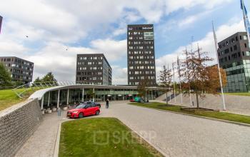 Exterior view of the office to rent at Papendorpseweg 95-97, Utrecht Papendorp, featuring a spacious courtyard with people walking and cars parked.