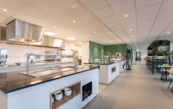 Spacious, modern office pantry at Van Deventerlaan 31-51, Utrecht Papendorp, with open food preparation area and seating, ideal for office space rental. People are serving food and dining.