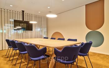 Bright conference room with modern wooden table, blue chairs, and a wall-mounted TV, perfect for office space rental or meetings at Van Deventerlaan 30-40, Utrecht Papendorp.