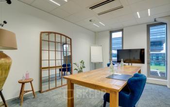 Modern office space rental at Orteliuslaan 850, Utrecht Papendorp with a stylish wooden table, comfortable chairs, and a large TV screen.