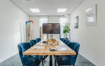 Bright office space rental at Orteliuslaan 850, Utrecht Papendorp, featuring a furnished conference room with a modern table, blue chairs, a large screen, and natural light through large windows.