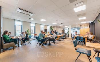 A bright and bustling office space at Orteliuslaan 850, Utrecht Papendorp, with groups of people engaged in discussions at tables. Ideal for office space rental.