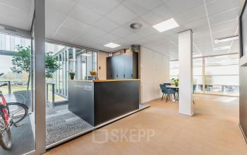 Modern office space rental in Utrecht Papendorp, Orteliuslaan 850, featuring a stylish reception area, furnished with a desk and seating. Bright natural light from large windows enhances the welcoming atmosphere.