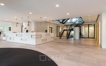 Modern reception area at Newtonlaan 115, Utrecht Rijnsweerd, featuring sleek white counters and a staircase.