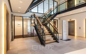 Modern office interior at Newtonlaan 115, Utrecht Rijnsweerd, featuring a staircase, elevator, and glass-walled workspaces. Ideal for office space rental.