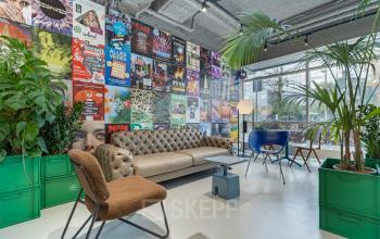 Lively office lounge at Daltonlaan 200, Utrecht Rijnsweerd, featuring colorful posters, a comfortable sofa, stylish chairs, and lush greenery, ideal for informal meetings. A unique twist for office space rental.