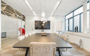 Modern conference room at Daltonlaan 200, Utrecht Rijnsweerd, featuring a long table, comfortable chairs, a flat-screen display, and ample natural light. Ideal office space rental opportunity.