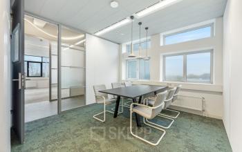 Modern office space rental on Daltonlaan 200 in Utrecht Rijnsweerd with a meeting table and chairs under hanging lights, featuring large windows for natural light.