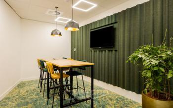 Modern conference room at Euclideslaan 51, Utrecht Rijnsweerd, featuring tall wooden table, colorful chairs, a large wall-mounted screen, and vibrant lighting. Ideal for office space rental.