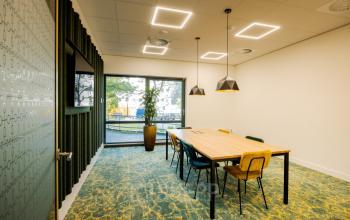 Bright conference room with a modern design at Euclideslaan 51, Utrecht Rijnsweerd. Features a long wooden table, colorful chairs, large window, and contemporary lighting, ideal for office space rental.