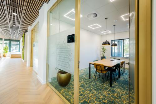 Modern conference room at Euclideslaan 51, Utrecht Rijnsweerd featuring a large wooden table, green-patterned carpet, glass walls, and abundant natural light. Ideal office space rental.