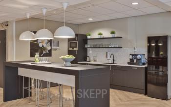 Modern office pantry in Niasstraat 1, Utrecht West, equipped with sleek black cabinets, a bar-style counter, and contemporary lighting, ideal for office space rental with functional amenities.