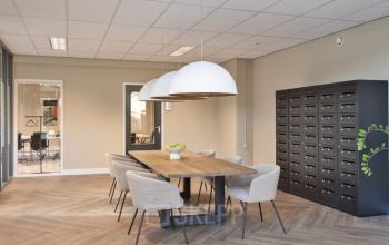 Modern workspace at Niasstraat 1 1 in Utrecht West featuring a large wooden table with comfortable chairs, pendant lighting, and a wall of mail slots suitable for office space rental.