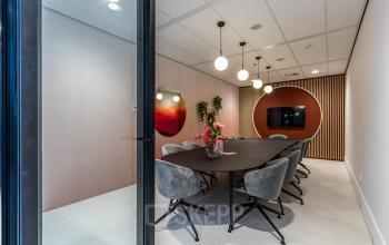 Modern conference room with a long table and stylish chairs, ready for office to rent in Utrecht South. Includes a TV screen and decorative elements.