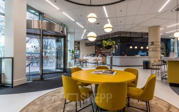 Modern office with round yellow table and chairs, attractive lighting, and reception area in the background, perfect for rent office space in Utrecht South.