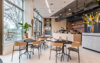 Furnished office space with modern decor and seating in Utrecht South, featuring a counter and several chairs and tables near large windows.