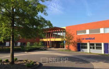 Exterior of the office building located at Kerkhofstraat 21, Valkenswaard, showing a modern red brick facade with large windows and a tree in the foreground.