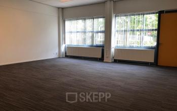 Empty office space with large windows and carpeted floor located at Kerkhofstraat 21, Valkenswaard.