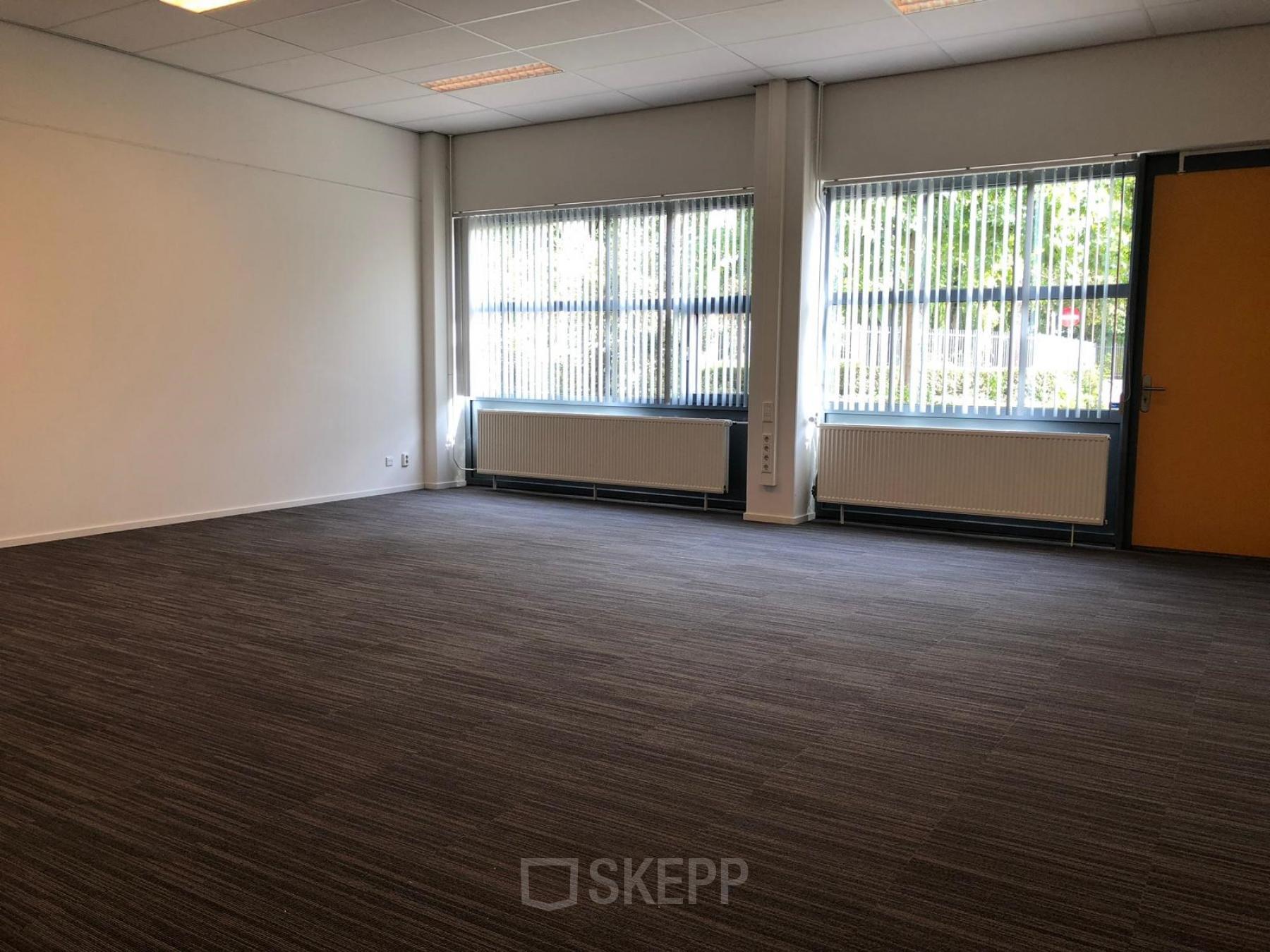 Empty office space with large windows and carpeted floor located at Kerkhofstraat 21, Valkenswaard.