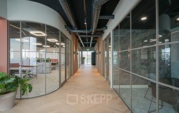 Modern hallway with glass partition walls in office space rental at Doornhoek 3745, Veghel. Visible workspaces through the glass feature bright lighting and sleek design, creating an inviting atmosphere for professionals.