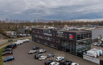 Exterior of modern office building at Doornhoek 3745, Veghel, featuring parking spaces and visible company logos, ideal for office space rental. Surrounding area includes other commercial buildings and greenery.