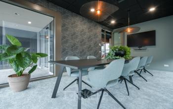 Modern conference room at Doornhoek 3745, Veghel, featuring sleek grey chairs, a large meeting table, and a wall-mounted TV, ideal for office space rental.