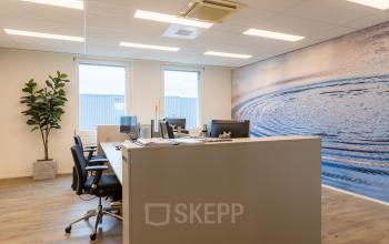 Contemporary office space located at Costerweg 5, Veghel, featuring modern workstations with ergonomic chairs and a stylish ocean mural. Ideal for office space rental, offering a comfortable work environment.